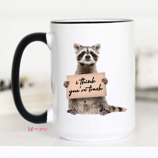 15 oz mug. Black handle and rim. Image of a raccoon holding a sign "i think you're trash"